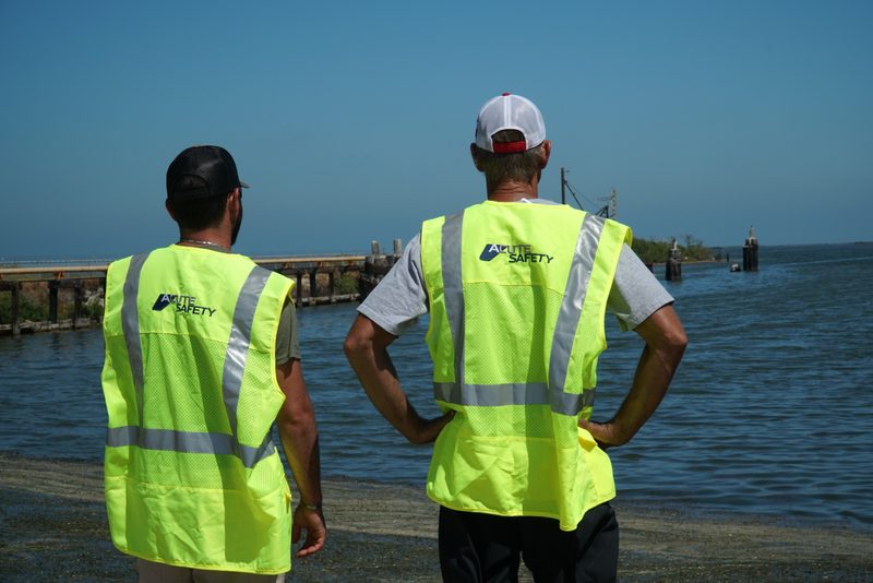 Two Acute Safety reps in hi-vis vests on the shoreline in Rockport, Texas